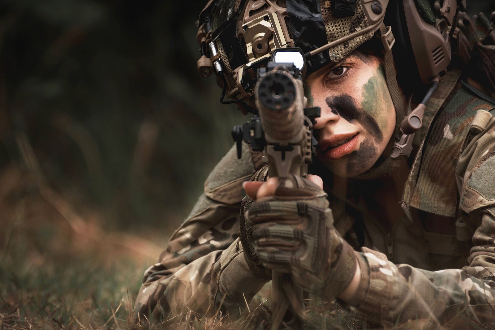 A player in camouflage and face paint lying prone and aiming a marker